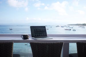 Serene beach view workspace in Bali with a laptop and coffee mug. Perfect for remote work inspiration.
