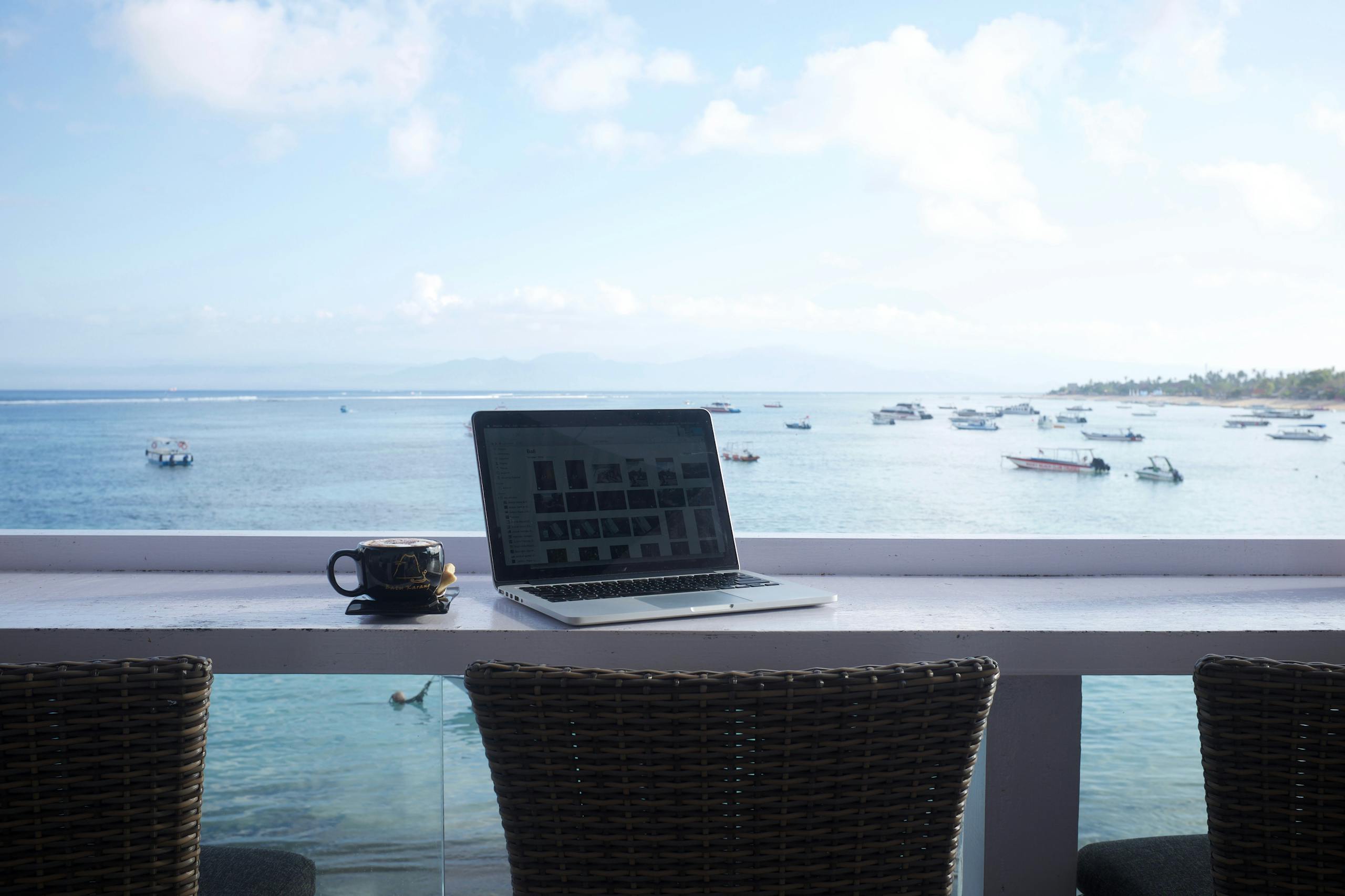 Serene beach view workspace in Bali with a laptop and coffee mug. Perfect for remote work inspiration.
